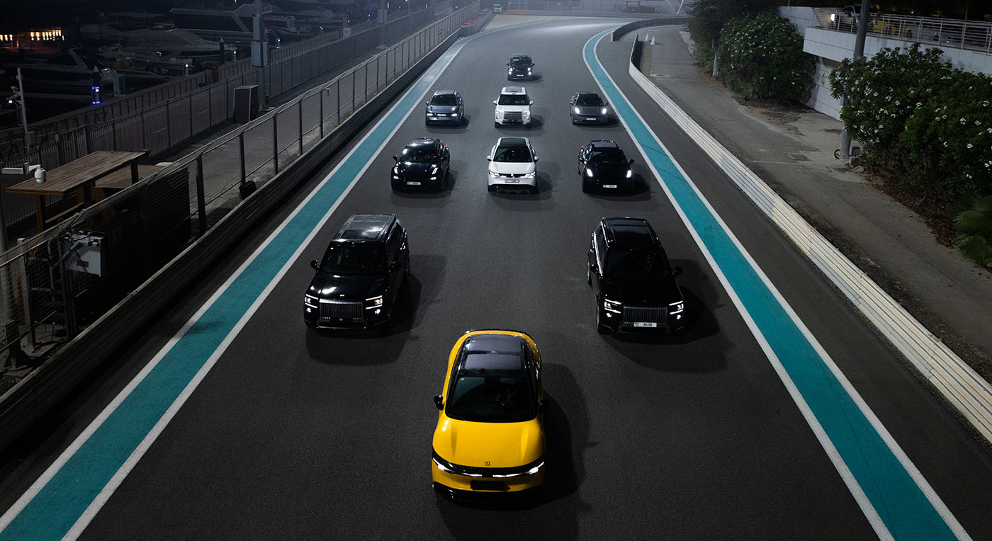 Overhead view of a group of electric cars driving in formation led by a bright yellow sedan on a night track.